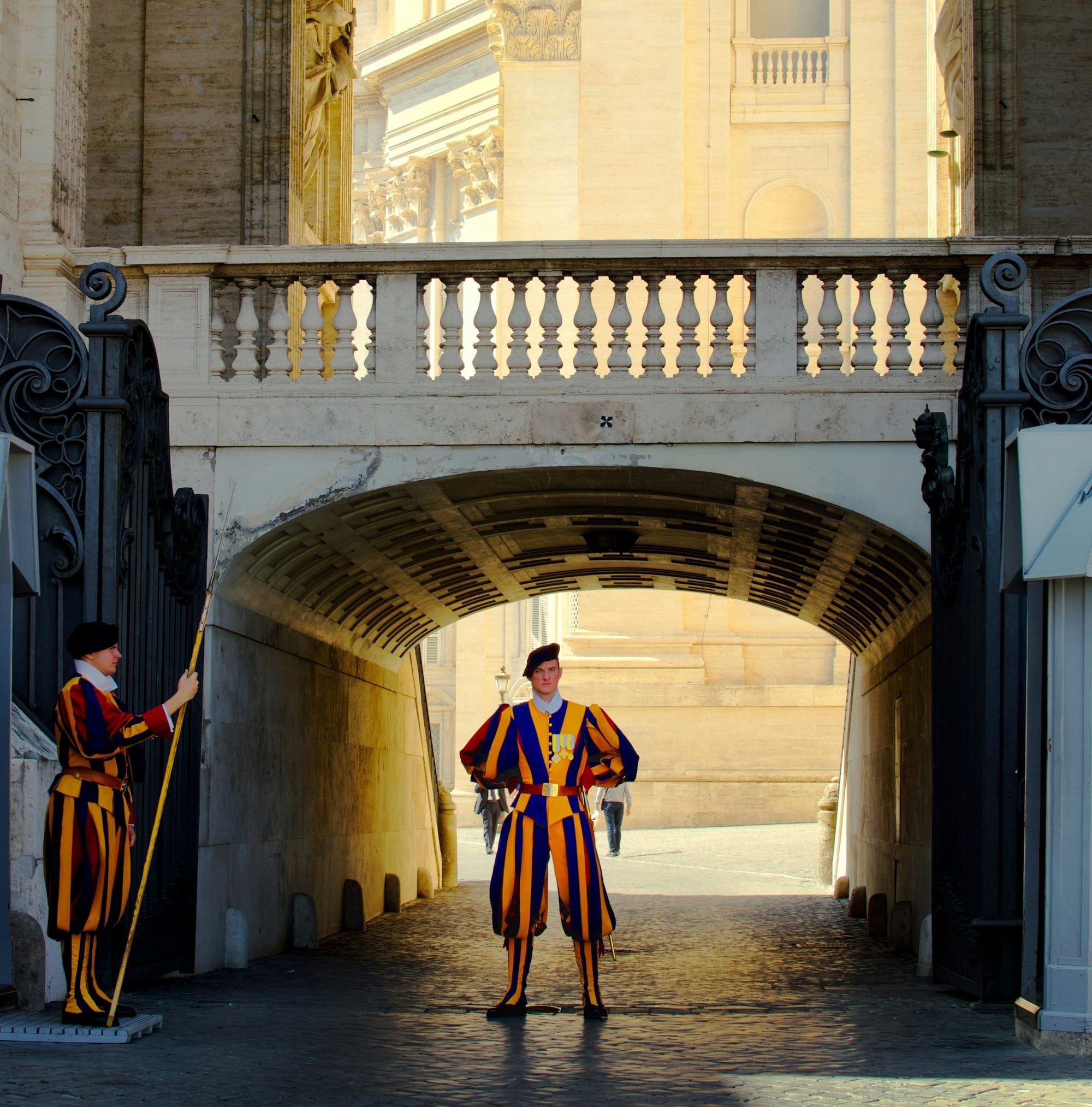 Two Swiss Guards in striped uniforms standing at an archway gate in Vatican City