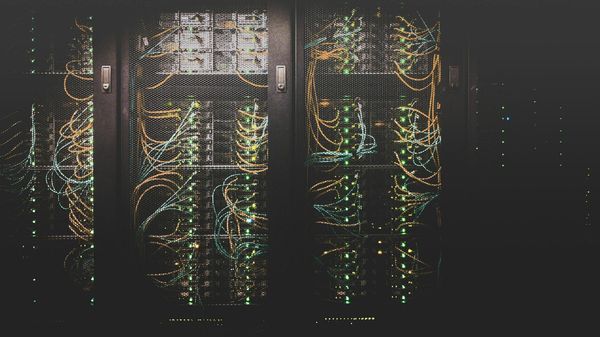 Rows of server racks in a dark data center, with orange and blue network cables and green status lights