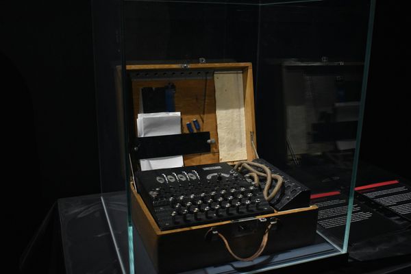 A wartime Enigma cipher machine in a wooden case, displayed inside a glass museum vitrine