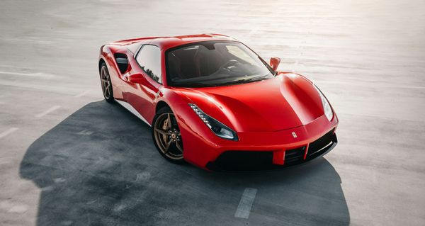 A red Ferrari sports car photographed from the front on a plain grey concrete floor