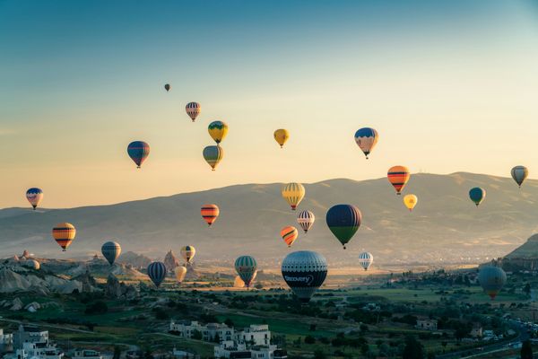 Dozens of hot air balloons drifting over a wide valley at sunrise