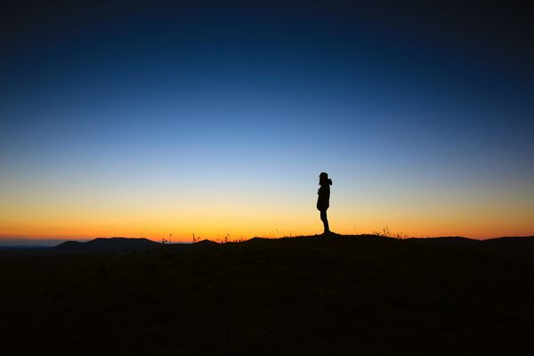 A lone figure standing in silhouette on a ridge against a deep blue and orange sunset sky